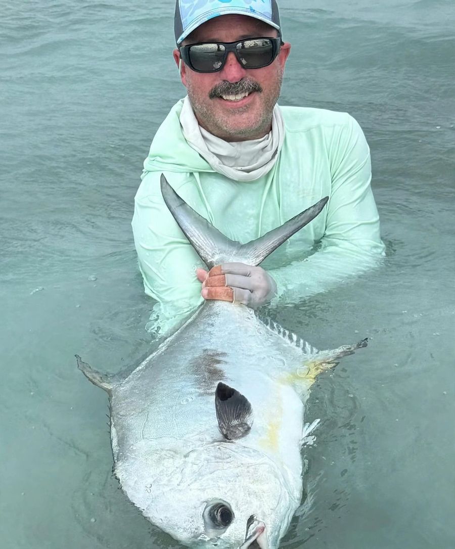 Angler holding a large permit in shallow turquoise water