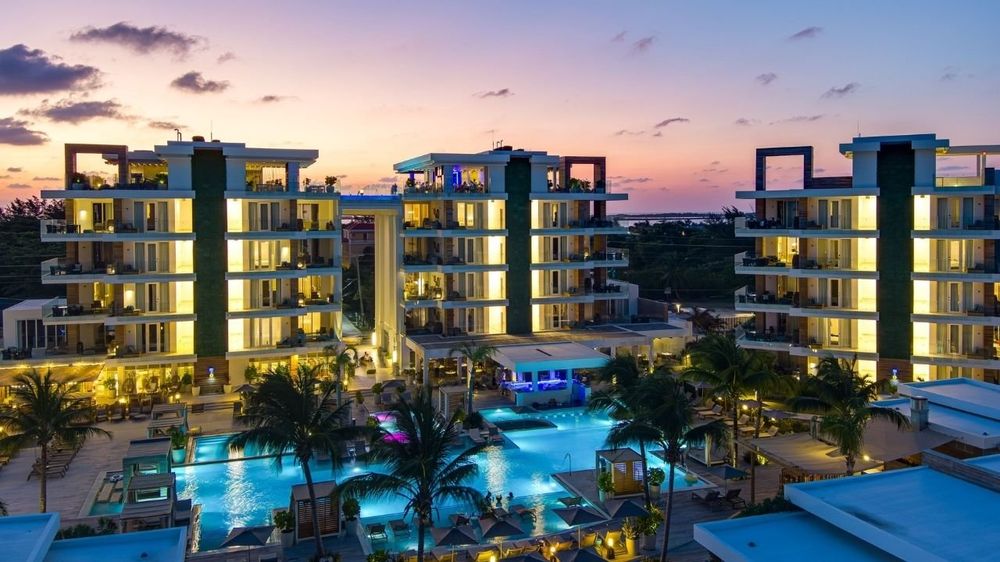 Beachfront resort at dusk on Ambergris Caye, its pool and balconies glowing under a pink sunset sky