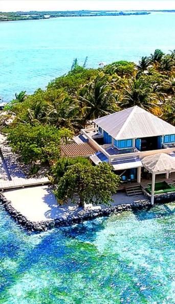 A waterfront house among palms on its own point of land, surrounded by clear turquoise water on Ambergris Caye